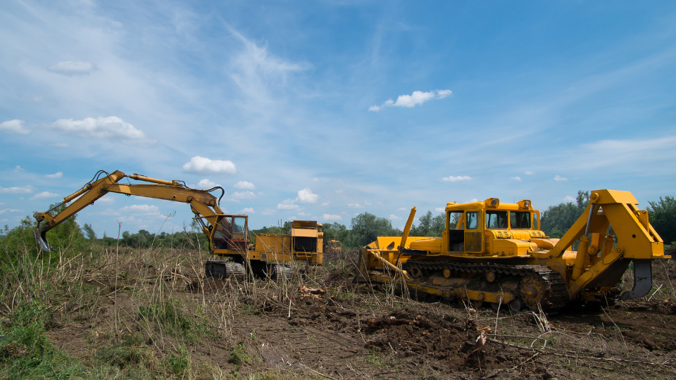Digger and bulldozer clearing forest land.