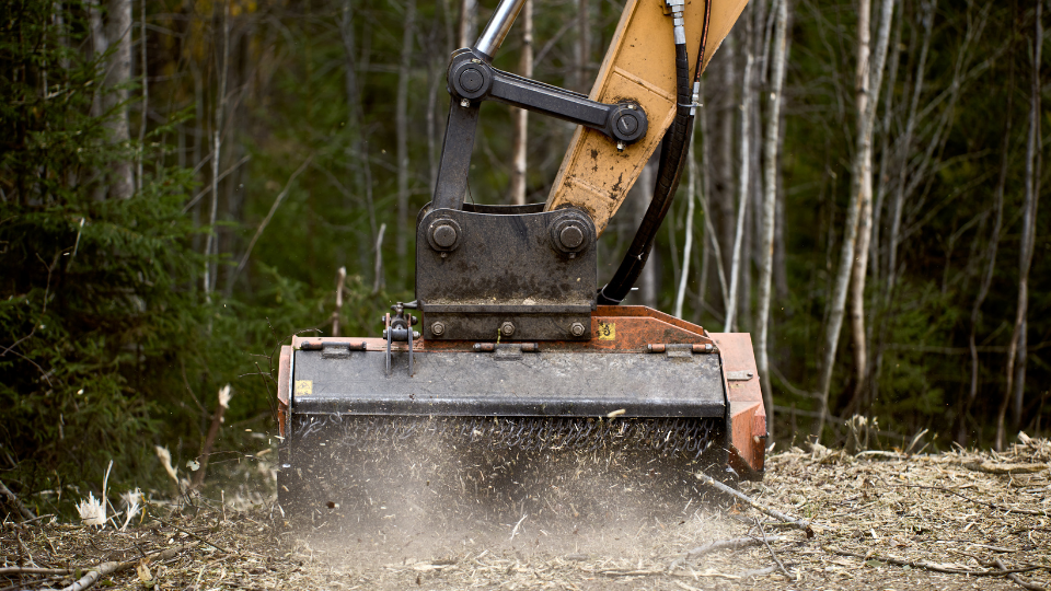 Attachable excavator forestry mulching head destroys roadside vegetation.